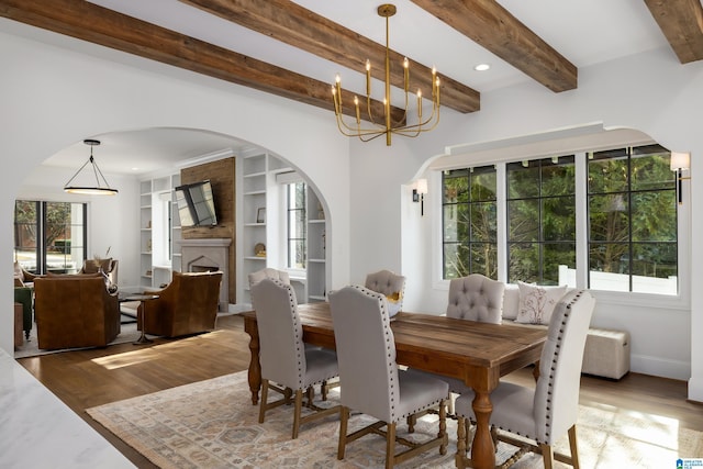 dining space with wood-type flooring, beamed ceiling, a notable chandelier, a fireplace, and built in features