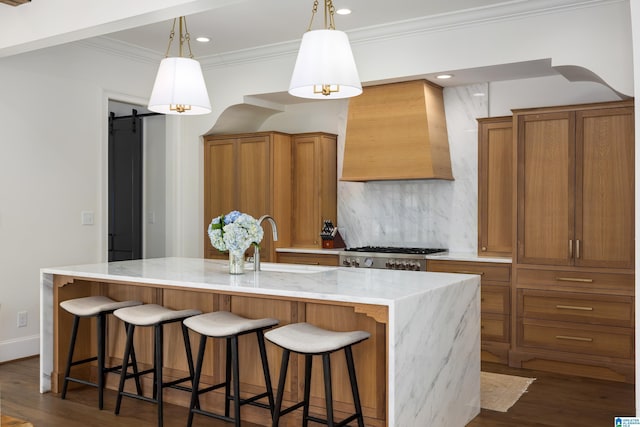 kitchen featuring premium range hood, an island with sink, a barn door, backsplash, and stove