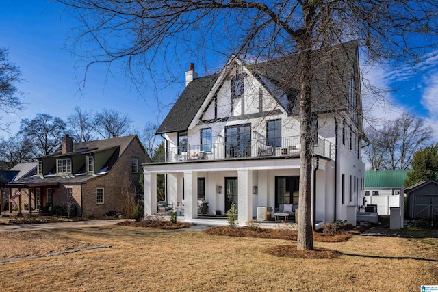 view of front of home with a front yard, covered porch, a balcony, and a storage unit