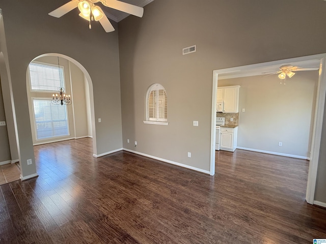 unfurnished room with a towering ceiling, dark hardwood / wood-style flooring, and ceiling fan with notable chandelier