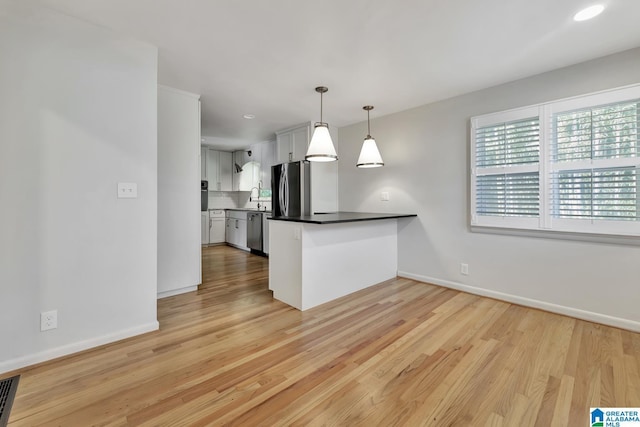 kitchen featuring decorative light fixtures, white cabinets, light wood-type flooring, backsplash, and appliances with stainless steel finishes