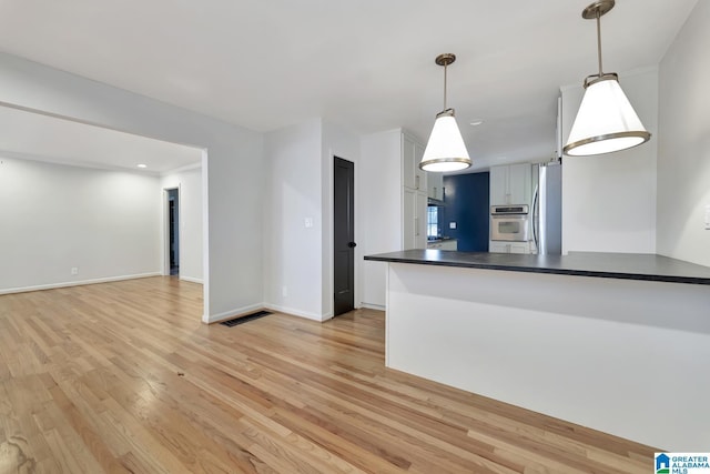 kitchen with kitchen peninsula, pendant lighting, stainless steel fridge with ice dispenser, and light hardwood / wood-style flooring