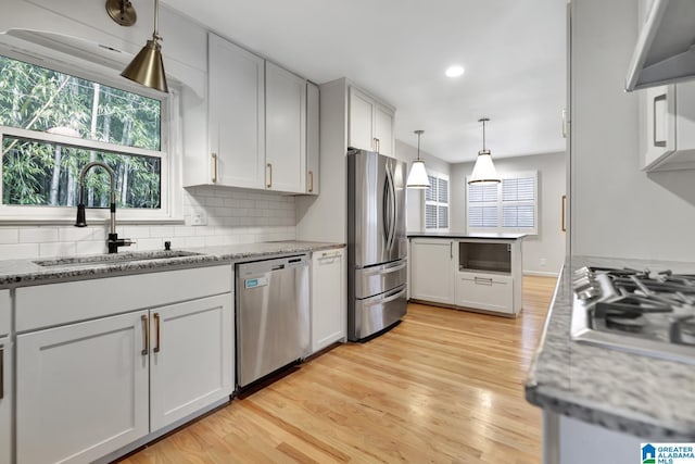 kitchen featuring appliances with stainless steel finishes, light hardwood / wood-style floors, light stone countertops, and sink