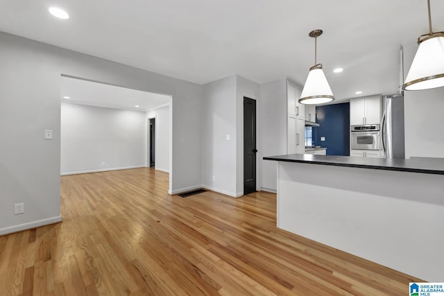 kitchen with white cabinets, light wood-type flooring, appliances with stainless steel finishes, and pendant lighting