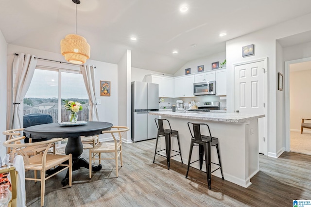 kitchen with white cabinetry, hanging light fixtures, stainless steel appliances, a center island with sink, and light wood-type flooring