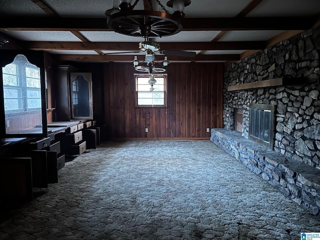 carpeted living room featuring beam ceiling, a stone fireplace, a notable chandelier, wood walls, and a textured ceiling