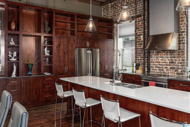 kitchen featuring sink, hanging light fixtures, appliances with stainless steel finishes, wall chimney exhaust hood, and brick wall