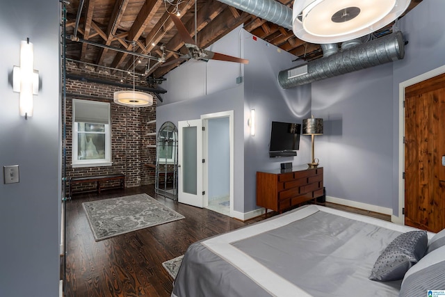 bedroom featuring beam ceiling, dark hardwood / wood-style flooring, brick wall, and a towering ceiling