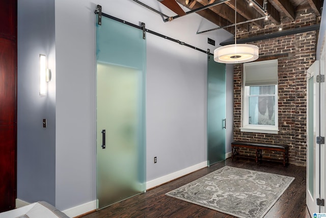 hall with dark wood-type flooring, brick wall, and a barn door