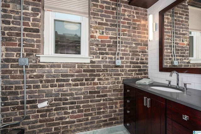 bathroom featuring brick wall, vanity, and tasteful backsplash