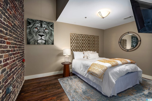 bedroom featuring brick wall and dark hardwood / wood-style flooring