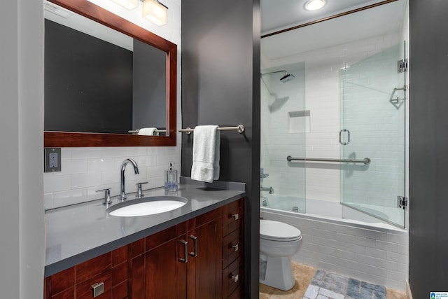 full bathroom with combined bath / shower with glass door, vanity, backsplash, and toilet