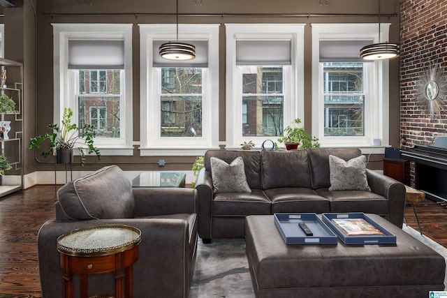 living room with dark wood-type flooring, brick wall, and a healthy amount of sunlight