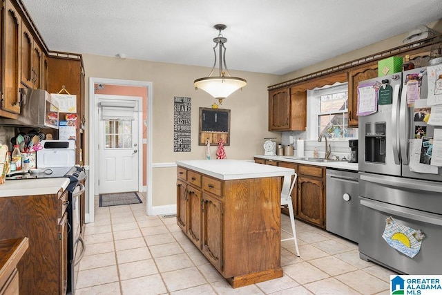 kitchen with sink, stainless steel appliances, light tile patterned floors, decorative light fixtures, and a kitchen island