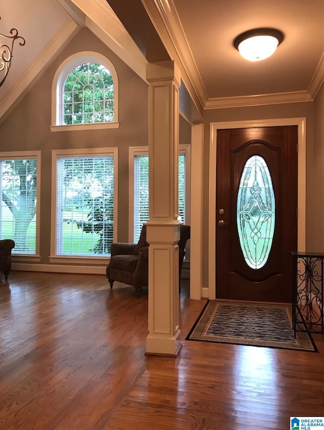 foyer entrance with decorative columns, dark wood-type flooring, lofted ceiling, and ornamental molding