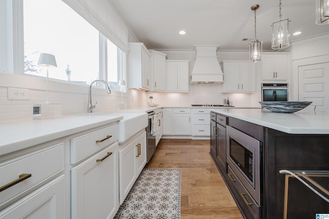 kitchen featuring custom exhaust hood, sink, light wood-type flooring, white cabinetry, and stainless steel appliances