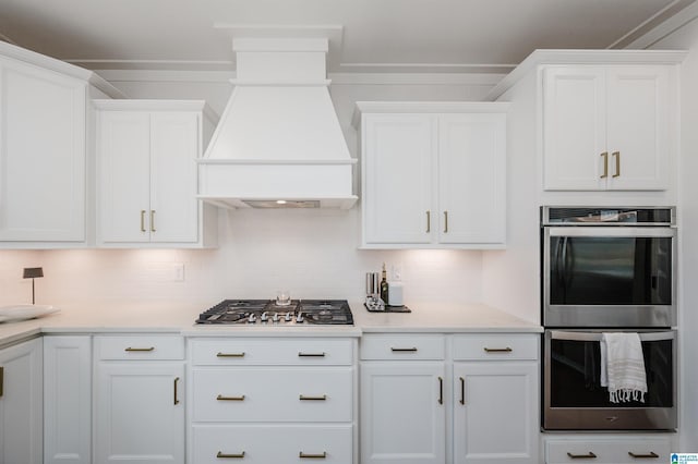 kitchen featuring premium range hood, backsplash, white cabinets, and stainless steel appliances