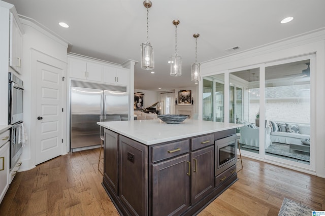 kitchen with decorative light fixtures, white cabinetry, a kitchen island, built in appliances, and dark brown cabinetry