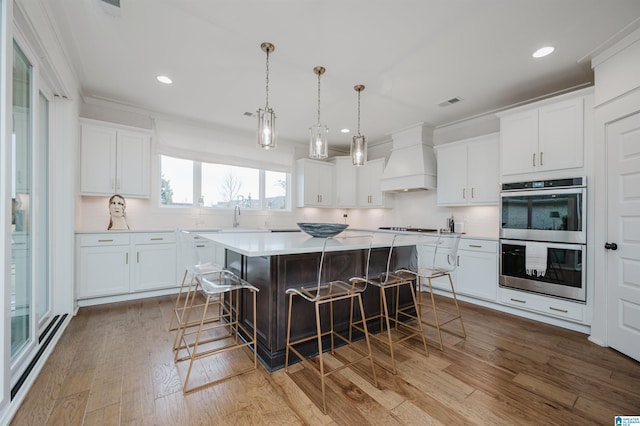 kitchen with white cabinets, a center island, double oven, premium range hood, and a breakfast bar area