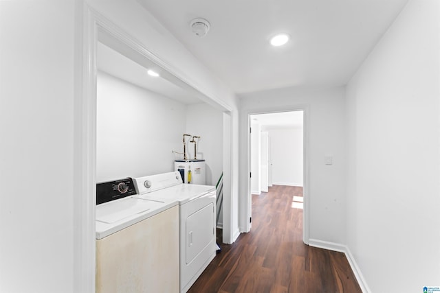 clothes washing area with washing machine and clothes dryer, electric water heater, and dark hardwood / wood-style flooring