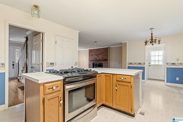 kitchen featuring decorative light fixtures, stainless steel range with gas cooktop, an inviting chandelier, light hardwood / wood-style floors, and a kitchen island