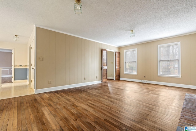 empty room featuring hardwood / wood-style flooring, a textured ceiling, wooden walls, and ornamental molding