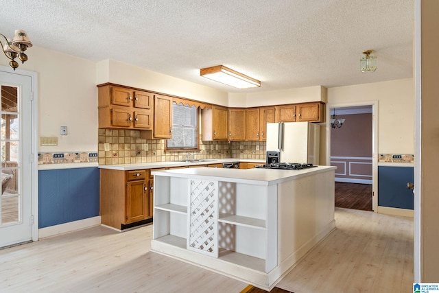 kitchen with a textured ceiling, light wood-type flooring, tasteful backsplash, and white fridge with ice dispenser