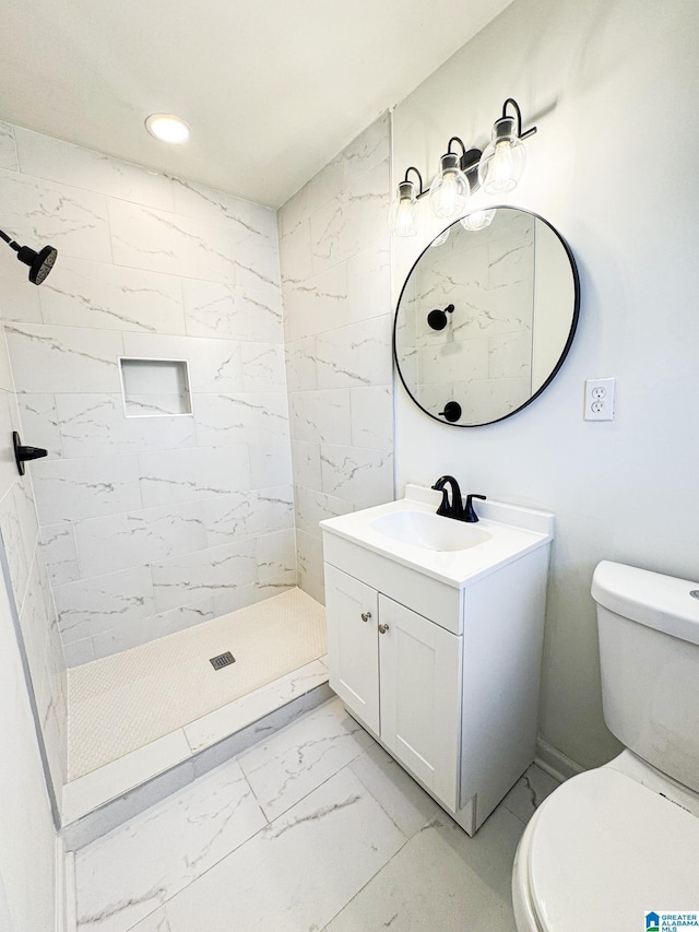 bathroom with toilet, tiled shower, and vanity