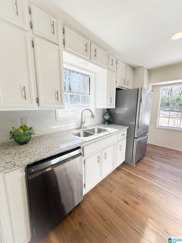 kitchen featuring white cabinetry, light hardwood / wood-style floors, appliances with stainless steel finishes, light stone countertops, and sink