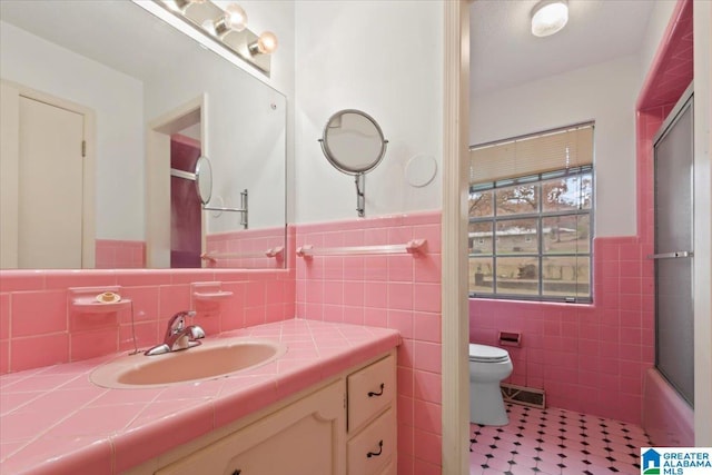 full bathroom with vanity, toilet, tile walls, and combined bath / shower with glass door