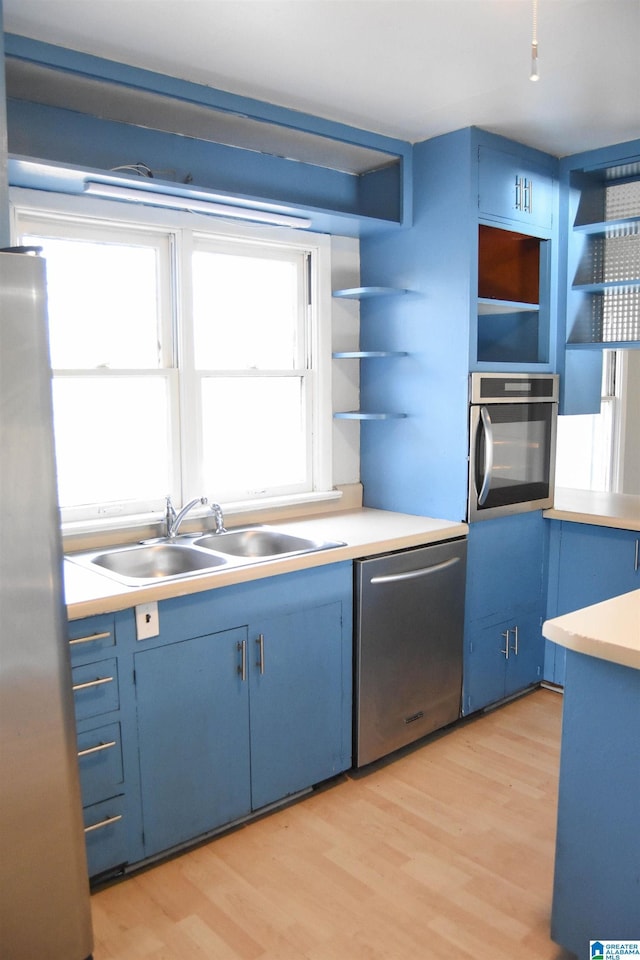 kitchen with blue cabinetry, stainless steel appliances, light hardwood / wood-style flooring, and sink