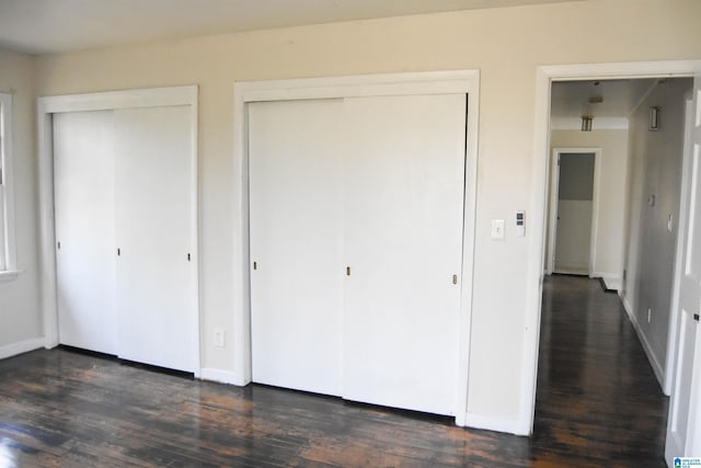 unfurnished bedroom with multiple closets and dark hardwood / wood-style floors