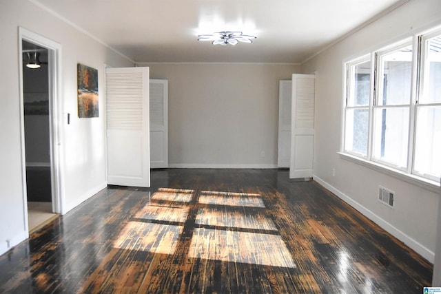 spare room with a healthy amount of sunlight, crown molding, and dark wood-type flooring