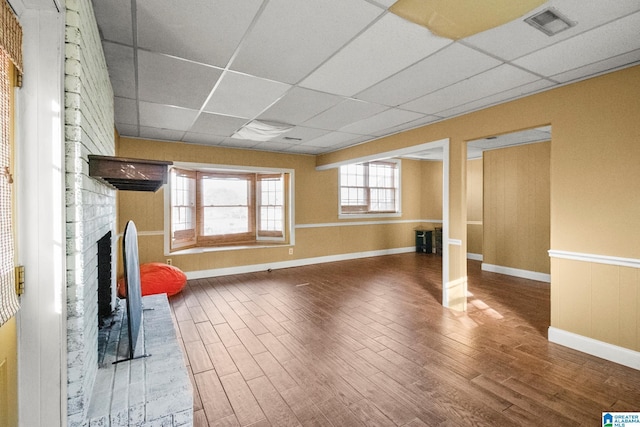 basement with a paneled ceiling, hardwood / wood-style flooring, and a brick fireplace