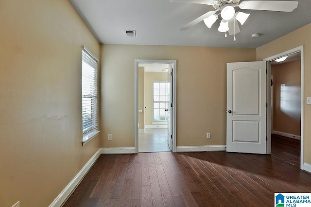 unfurnished bedroom featuring connected bathroom, multiple windows, ceiling fan, and dark wood-type flooring