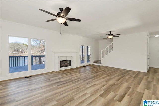 unfurnished living room with light wood-type flooring, a premium fireplace, ornamental molding, and ceiling fan