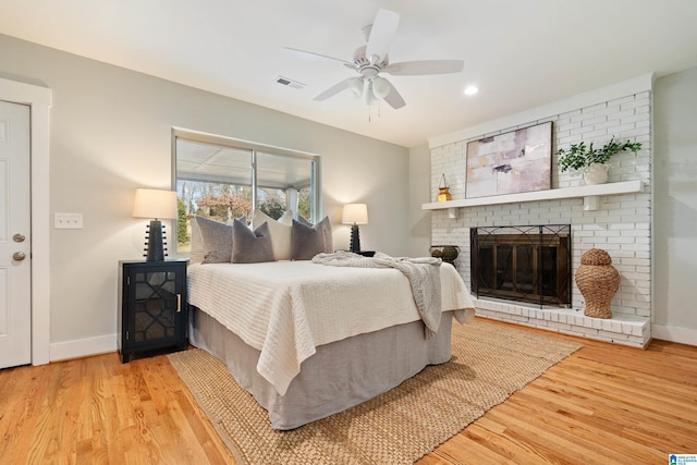 bedroom with a fireplace, ceiling fan, and light hardwood / wood-style floors