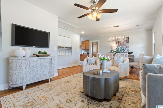 living room featuring ceiling fan with notable chandelier and light hardwood / wood-style flooring