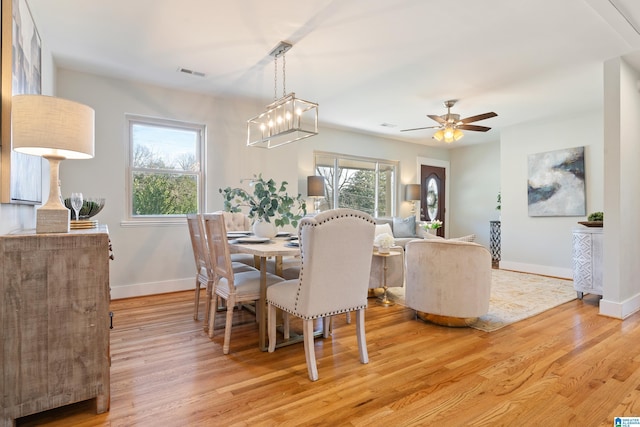 dining space with light hardwood / wood-style floors, a healthy amount of sunlight, and ceiling fan with notable chandelier