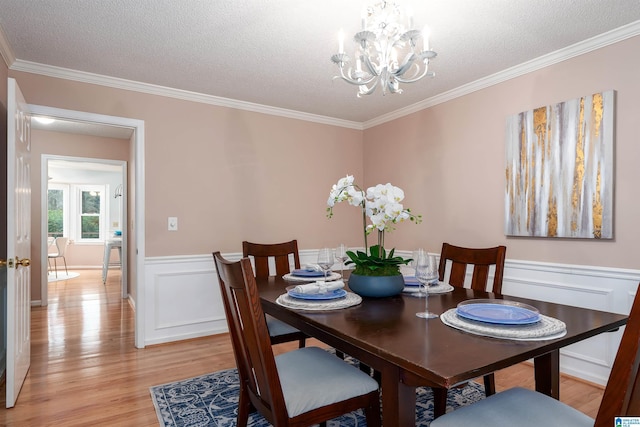 dining room with light hardwood / wood-style floors, ornamental molding, a textured ceiling, and an inviting chandelier