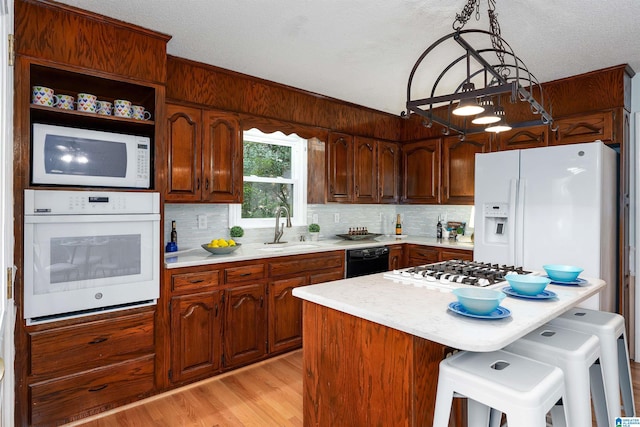 kitchen with white appliances, sink, a center island, light hardwood / wood-style floors, and hanging light fixtures