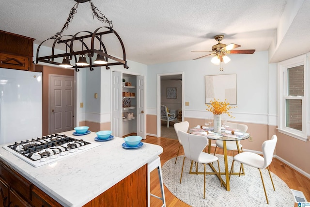 kitchen with a textured ceiling, ceiling fan with notable chandelier, light hardwood / wood-style floors, and white appliances