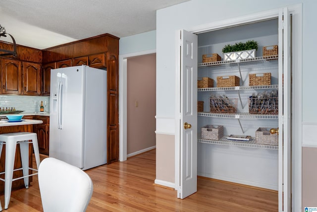 interior space featuring white refrigerator with ice dispenser, a textured ceiling, light hardwood / wood-style floors, and backsplash