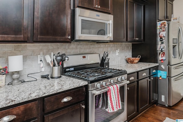 kitchen featuring light stone countertops, dark hardwood / wood-style flooring, decorative backsplash, dark brown cabinets, and appliances with stainless steel finishes