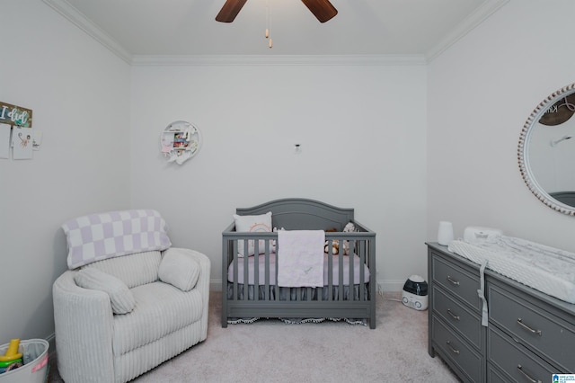 carpeted bedroom with a crib, ceiling fan, and ornamental molding