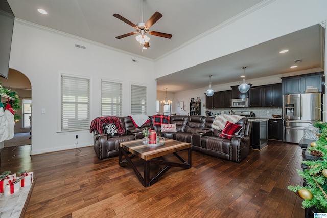 living room with ceiling fan with notable chandelier, crown molding, and dark wood-type flooring