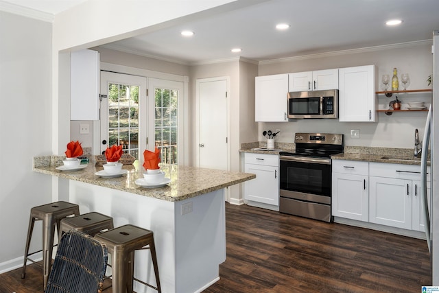 kitchen with white cabinets, light stone countertops, a breakfast bar area, and appliances with stainless steel finishes