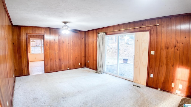 carpeted empty room featuring ceiling fan, ornamental molding, wooden walls, and a textured ceiling