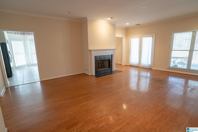 unfurnished living room with a tiled fireplace, wood-type flooring, and ornamental molding