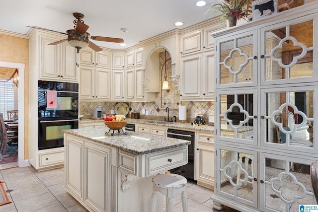 kitchen with sink, hanging light fixtures, cream cabinets, a kitchen island, and black appliances